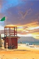green warning flag above lifeguard tower on beach
