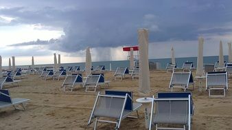 free chairs and folded umbrellas on beach at stormy weather