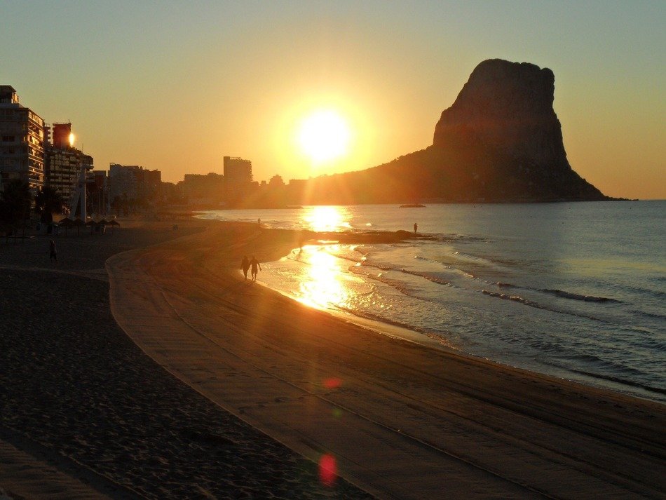beach, cliff and buildings on seashore at sunset
