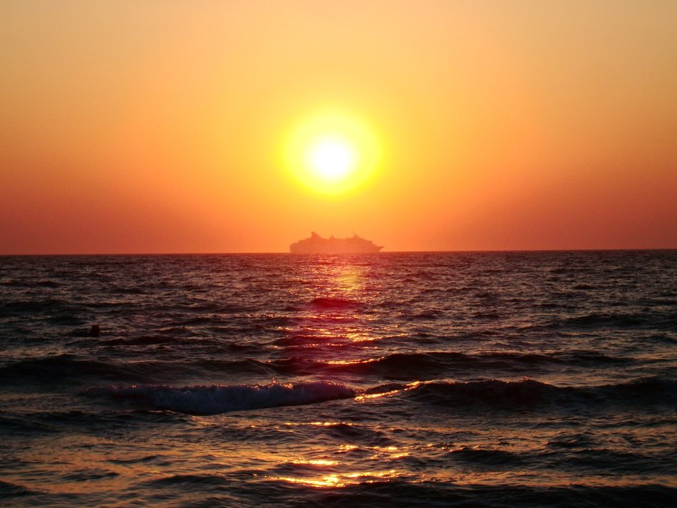 Beautiful and colorful sunset above the wavy water with the ship
