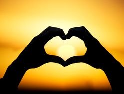 silhouette of a heart-shaped hand on a sunset background