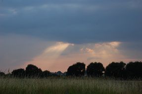 the sun's rays through the dark sky over a rural meadow