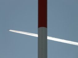 trail of an airplane in the sky behind a red and white pillar
