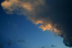 dark cloud with soft sunset colored edge in deep blue sky