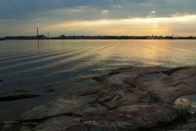 rocky coast at calm water and urban silhouettes at sunset sky, landscape