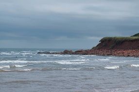 red cliff on sea shore at cloudy weather