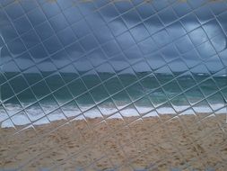 view of sand beach at sea through checked glass