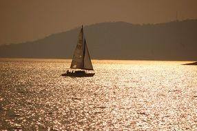 sailboat on the lake at colorful sunset and mountains in mist