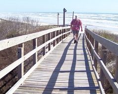 man walking away on boardwalk on beach