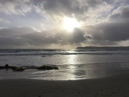 sun beams bursting through grey clouds at evening sky above water