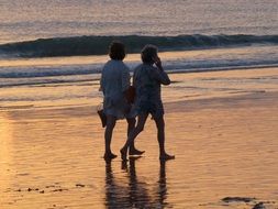 women walk along the beach at sunset