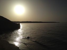 sunset, glossy sea at dark coastline