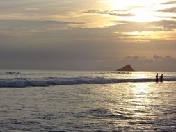 a couple of people in the water on the beach at dusk