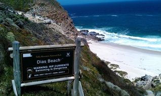 sign on the rocky coast with the sandy beach in south africa