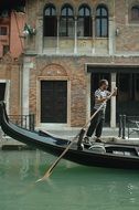 man with paddle in gondola on canal, italy, venice