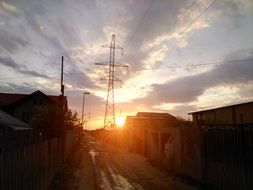 village and high-voltage tower on a background of orange sunset