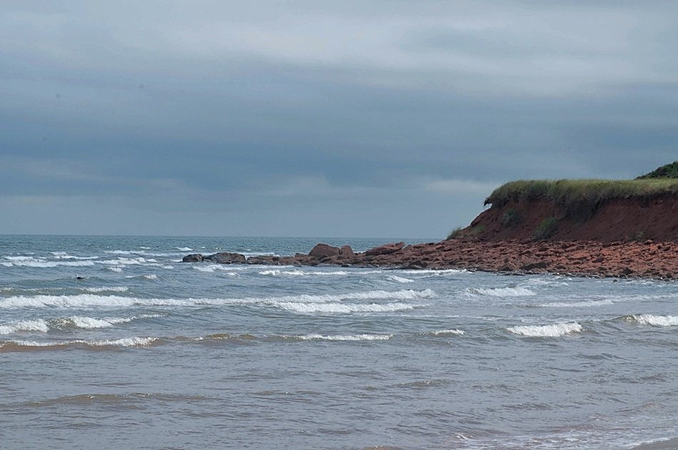 red cliff on sea shore at cloudy weather