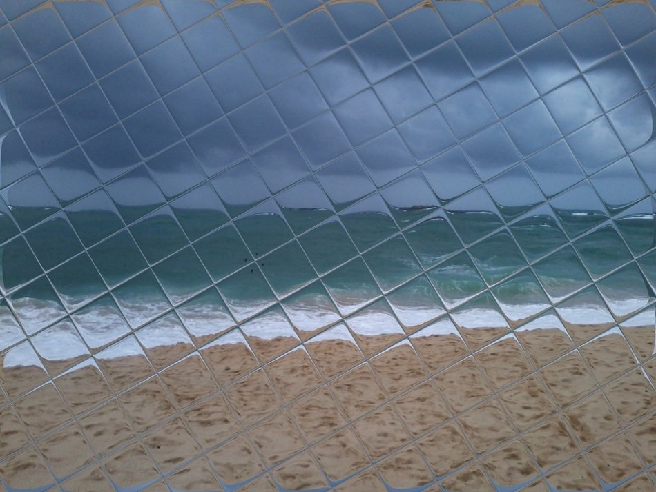 view of sand beach at sea through checked glass