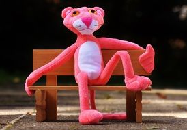 pink panther sitting on a wooden bench