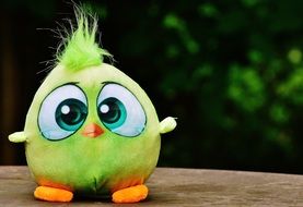 soft toy in the form of a bird with a sad look sitting on a rock on a background of green leaves