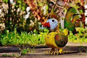 metallic element in the form of a rooster on an asphalt path in the garden