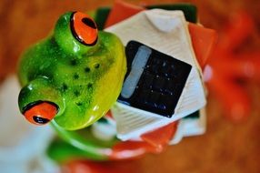 ceramic frog holds in paws a paper and a calculator