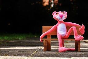 pink panther sitting on a wooden bench in the park