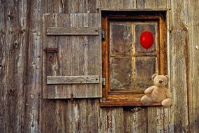Tteddy bear on the window of a wooden house