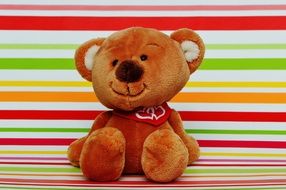 Teddy bear with a red handkerchief around his neck on a background of colored bands