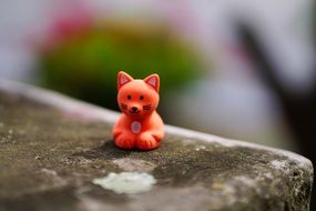 red toy in the form of a cat on a stone at blurred background