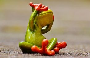 green frog sitting on the ground and closed her eyes paws