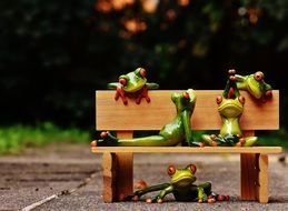 a lot of green frogs on a wooden bench