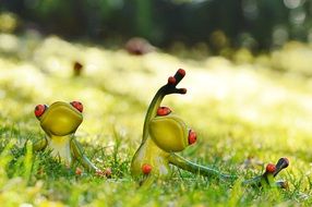 two ceramic frogs do yoga on the meadow in a blurred background