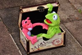 Green frog and pink panther are sitting in a box