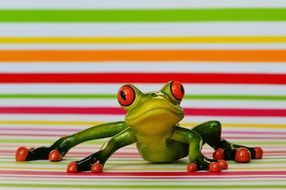 ceramic frog lying on a background of colored bands