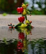 two toy frogs with red hearts on the shore of a pond