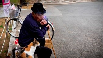 old man with a cigarette near a cat on the bench