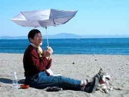 man under an umbrella on the beach and a dog