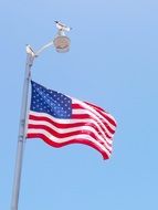 seagull sits on pile above Usa Flag winding at blue sky