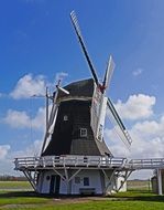 Beautiful windmill on the green field at blue sky background with white clouds