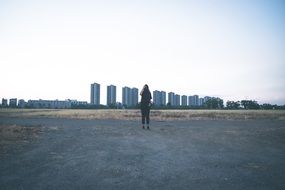 Alone Girl stands on road, distant buildings at background