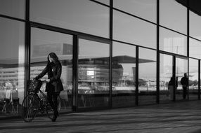 woman walking with bicycle along Modern Glass Facade