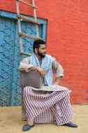 young Bearded Man in muslim clothing sits on ladder at colorful building