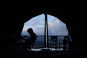 male Person sits on curtained balcony at evening