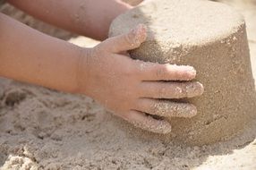 child making sand form on beach