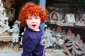 red-haired boy stands near toys