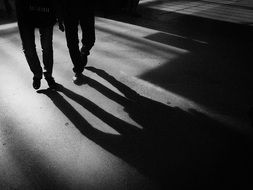 monochrome picture of people walk along the road near the shadow