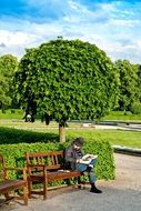 man is reading a newspaper at a park bench in Munich