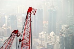 two red tower Cranes at foggy cityscape with skyscraper
