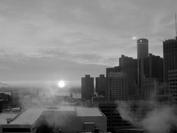 black and white photo of the sun rising near the houses